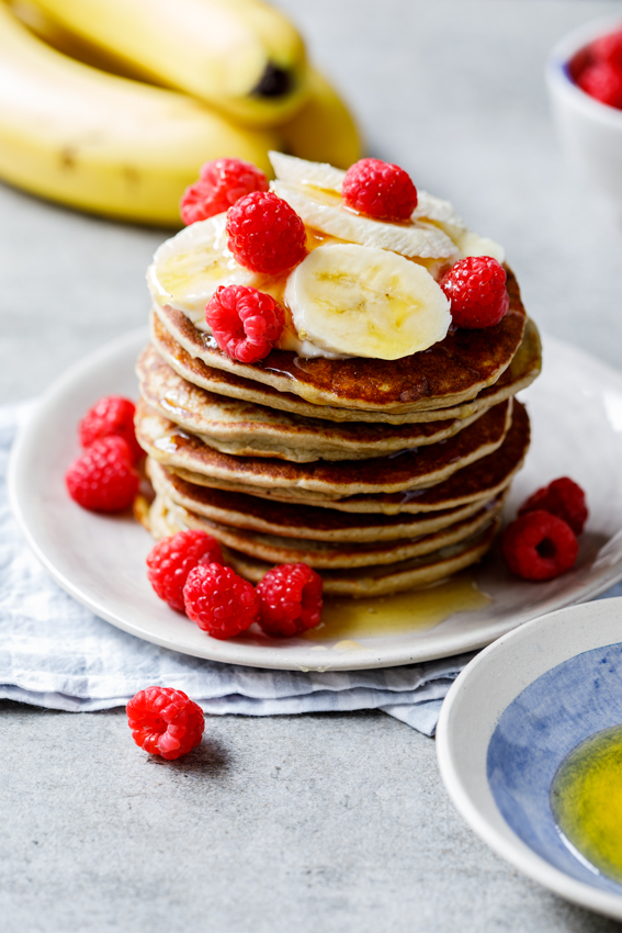 A stack of healthy banana oat pancakes topped with fresh banana and raspberries