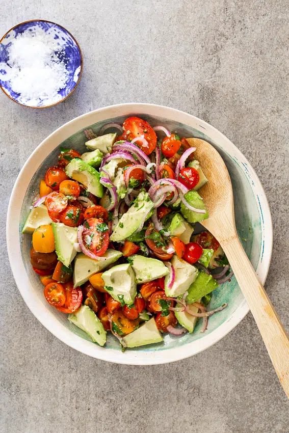 Tomato avocado salad in serving bowl with wooden spoon.