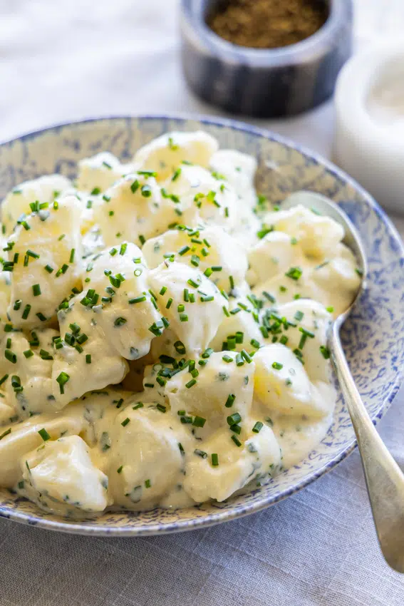 Creamy potato salad with fresh chives in a blue and white serving bowl.