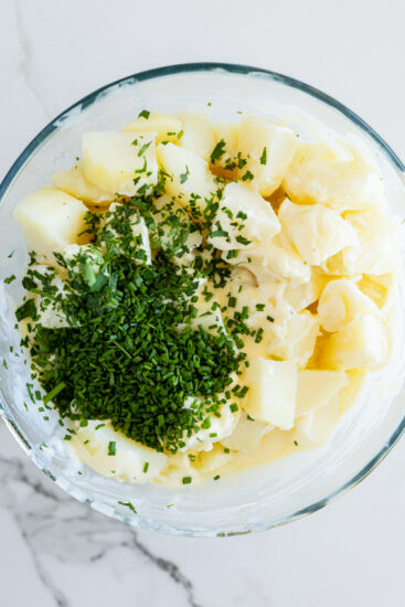 Potatoes, dressing and herbs in a glass bowl.