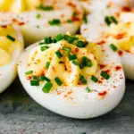 Classic deviled eggs garnished with paprika and chives on a serving plate.