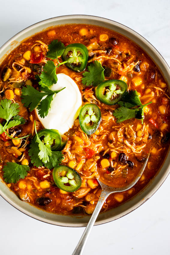 Spicy chicken black bean soup in serving bowl topped with sour cream, jalapenos and cilantro.