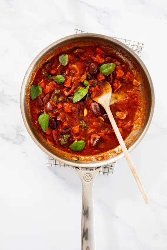 Puttanesca sauce in pan with fresh basil.