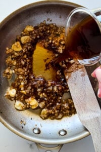 Beef stock poured into a hot pan with onions and garlic.