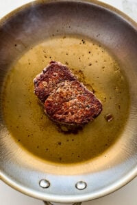 Seasoned steak in a hot pan.