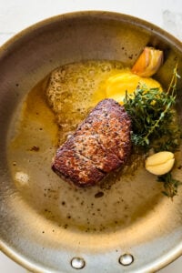 Butter and aromatics in a pan with a seared steak.