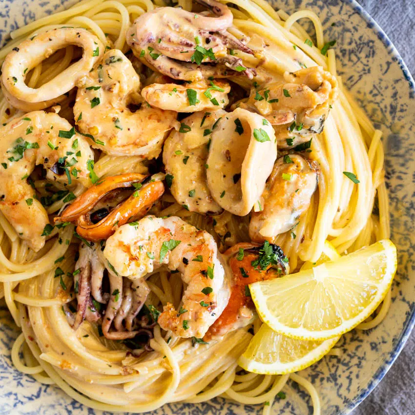 Creamy garlic seafood pasta with lemon in serving bowl.