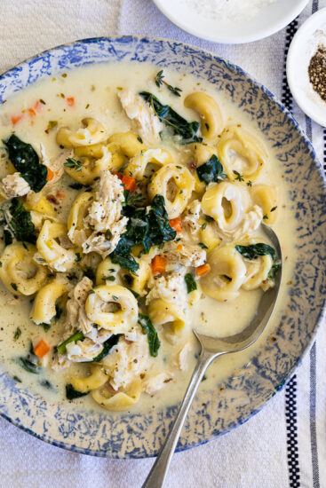 Creamy Chicken Tortellini Soup in blue and white bowl on tablecloth.