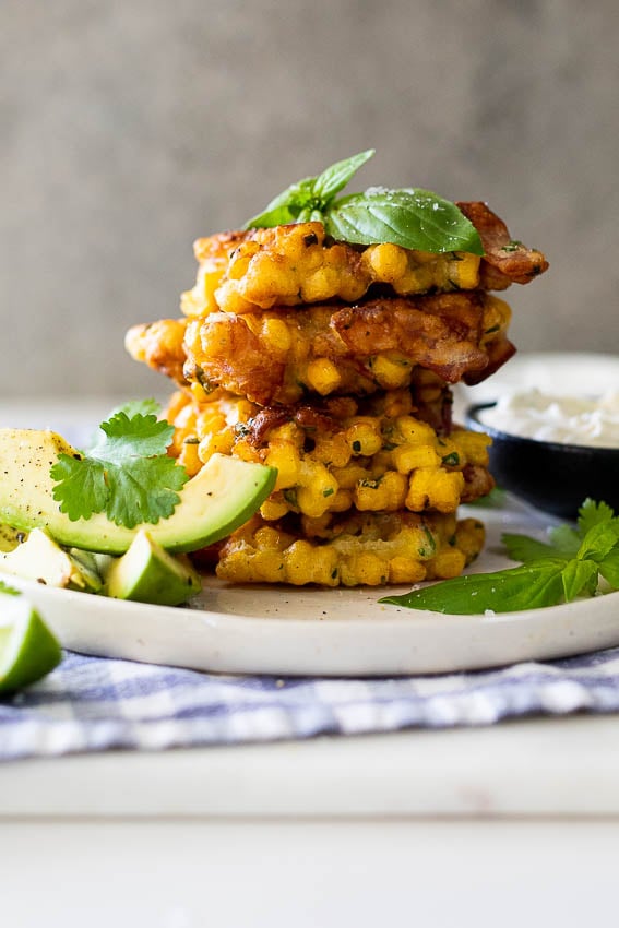 Chunky bacon corn fritters on a serving plate with avocado.