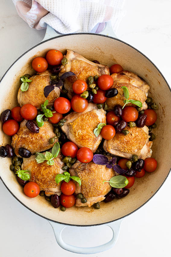 Chicken in pan with tomatoes, olives and capers.