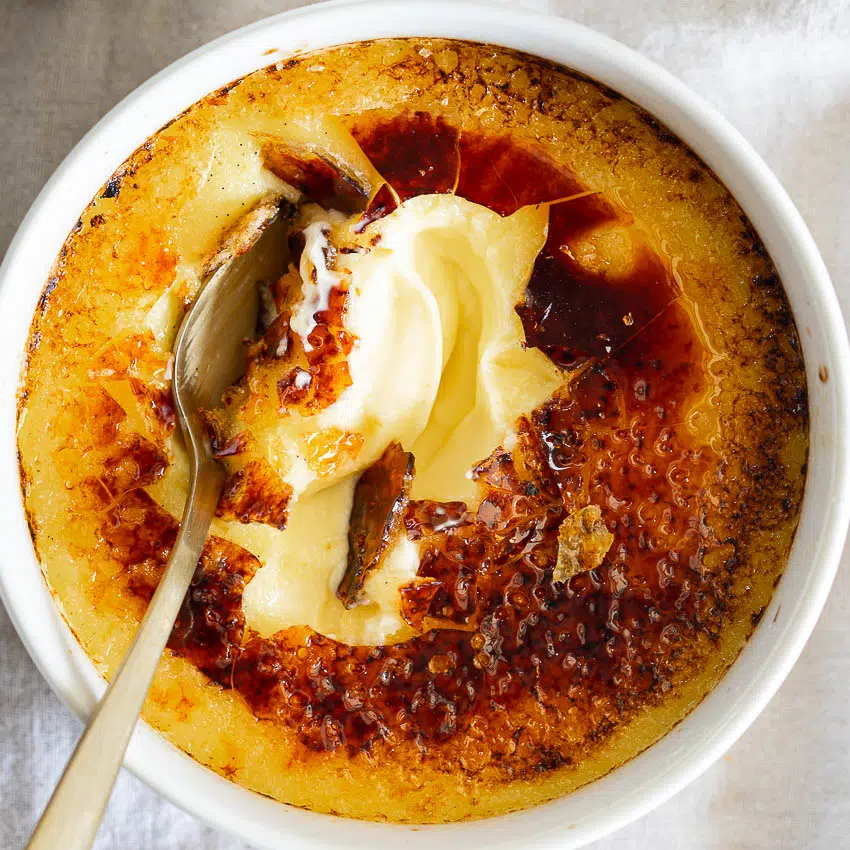Crème brûlée with perfectly smooth custard with a spoon cracked through.