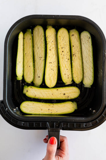 Raw zucchini in air fryer basket.