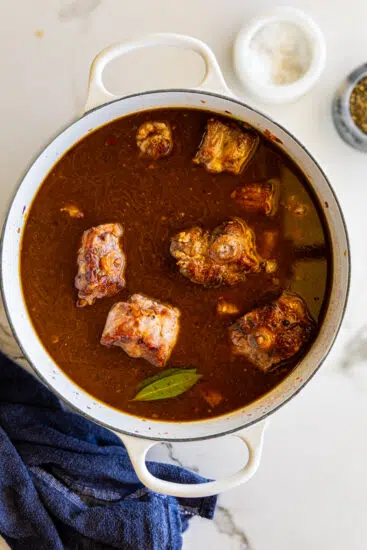 Oxtails in large pot with stock, wine and aromatics.