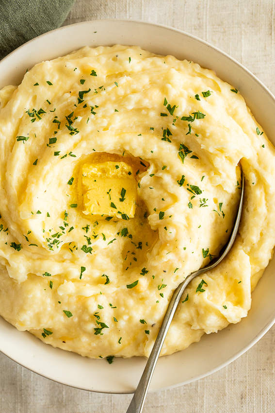 Cheesy mashed potatoes in serving bowl with butter.