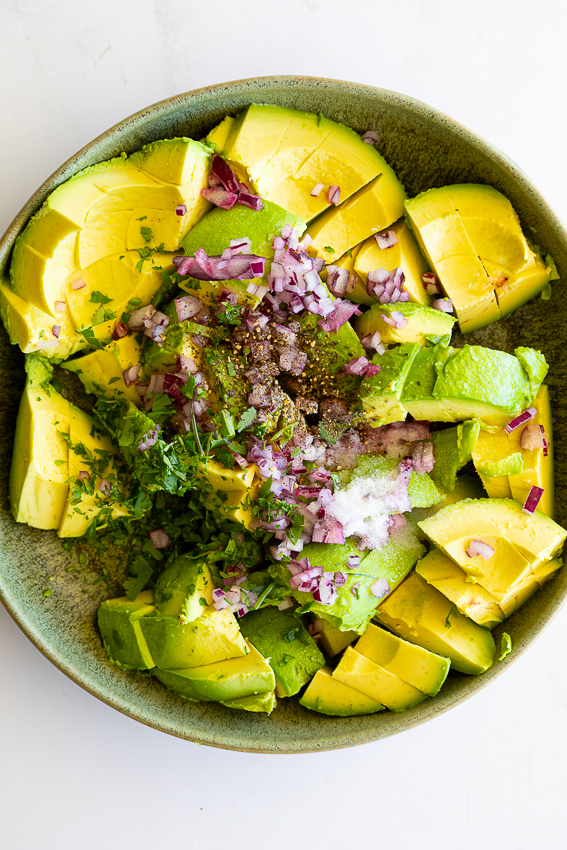 Avocado, red onion, cilantro and seasoning in bowl.