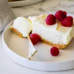 Easy no bake cheesecake served with fresh raspberries on a white plate.