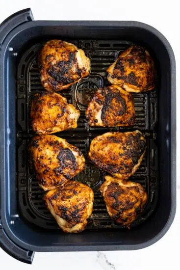 Cooked air fried chicken thighs in air fryer basket.