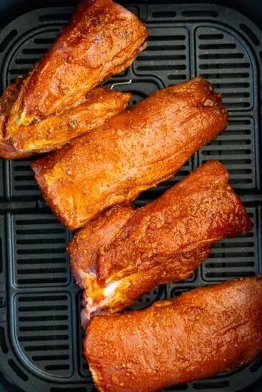 Seasoned pork tenderloin in air fryer basket.