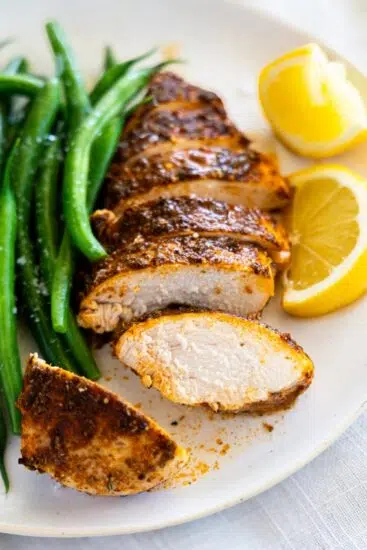 Baked Chicken Breast served with green beans and lemon wedges.
