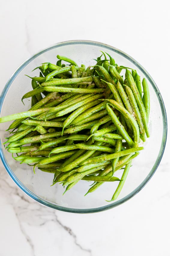 Trimmed green beans in bowl with olive oil and seasonings.