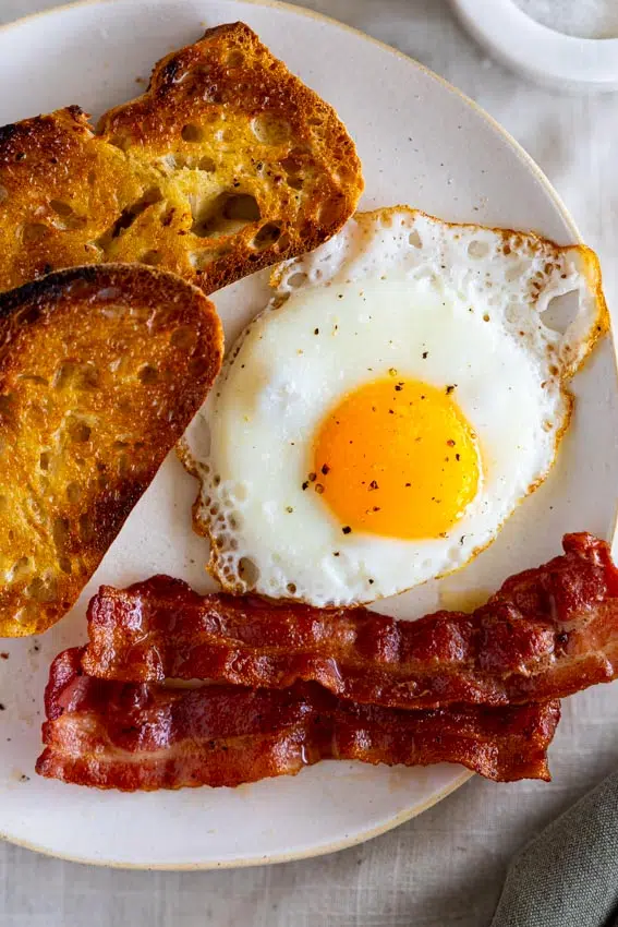 Fried eggs with bacon and toast on plate.