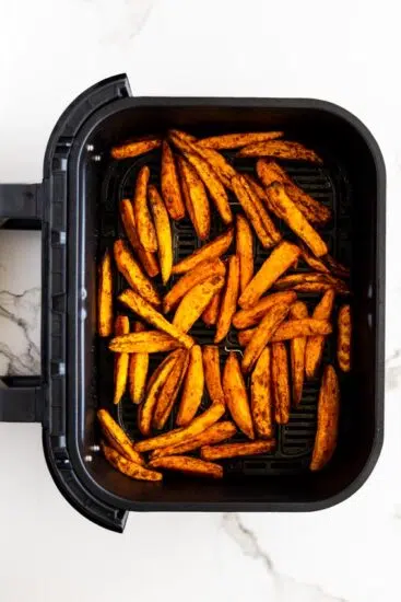 Air fried sweet potato wedges in air fryer basket.