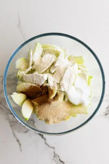 Apples, flour, sugar and cinnamon in mixing bowl.