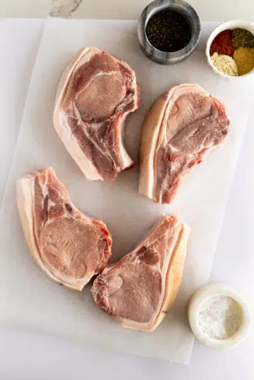 Raw pork chops on chopping board with spices