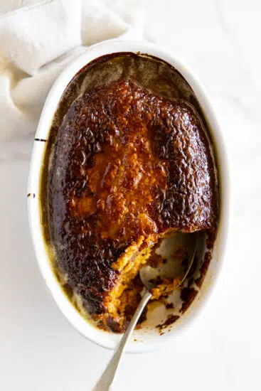 Baked malva pudding with syrup and serving spoon.