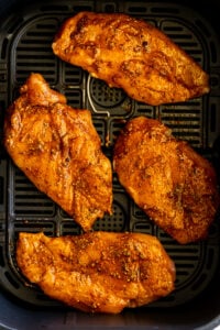 Seasoned chicken in air fryer basket.