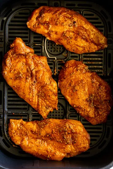 Seasoned chicken in air fryer basket.
