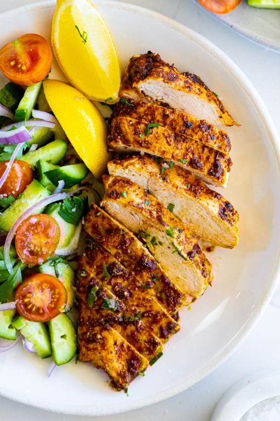 Juicy air fryer chicken breast on a white plate with salad.