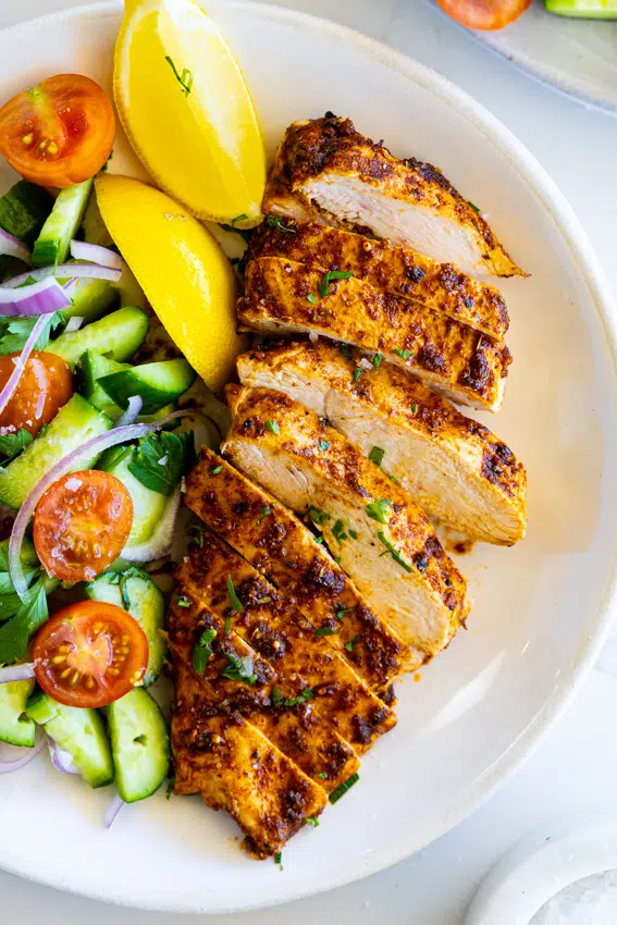 Juicy air fryer chicken breast on a white plate with salad.