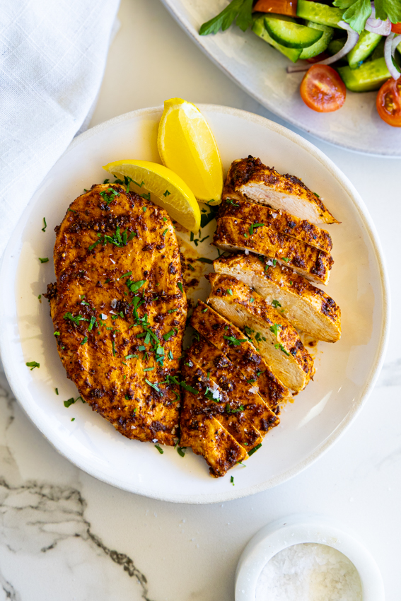 Air fryer chicken on a white plate with lemon wedges.