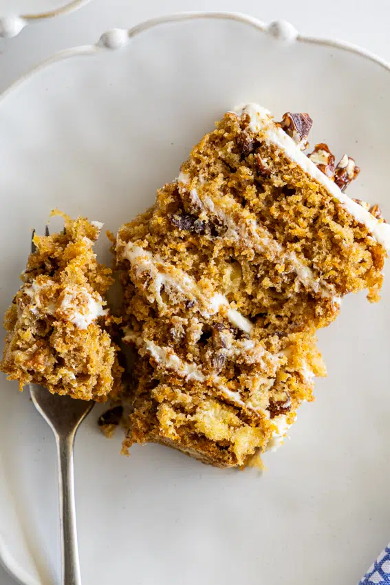 The best carrot cake layered with vanilla bean cream cheese frosting topped with pecan praline on a plate with a fork.