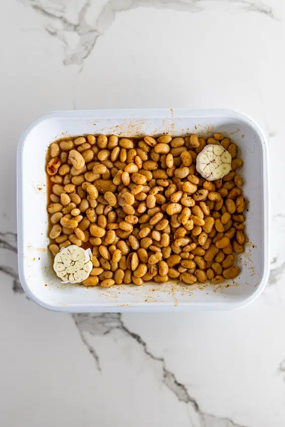 Beans and halved garlic bulbs in a baking dish.