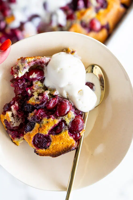 Cherry Cobbler in a serving bowl with vanilla ice cream and a gold spoon.