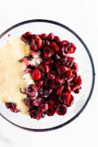 Pitted cherries in a mixing bowl with sugar, salt and almond essence.