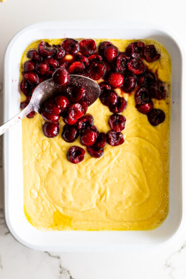Cherries spooned over cobbler batter in a white baking dish.