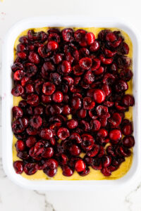 Macerated cherries on cobbler batter in a white baking dish.