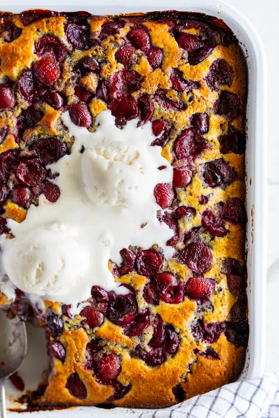 Cherry cobbler in baking dish topped with scoops of vanilla ice cream.