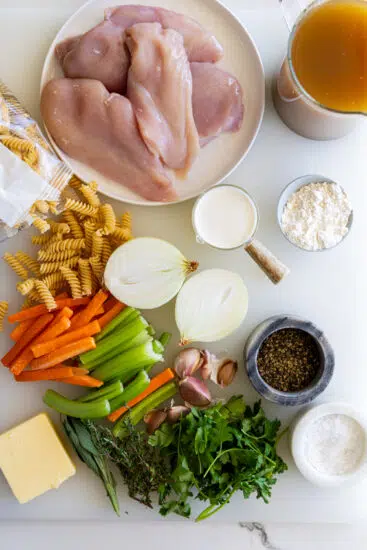 Ingredients for chicken noodle soup on a white surface.