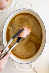 Chicken breasts put into chicken stock in white pot.