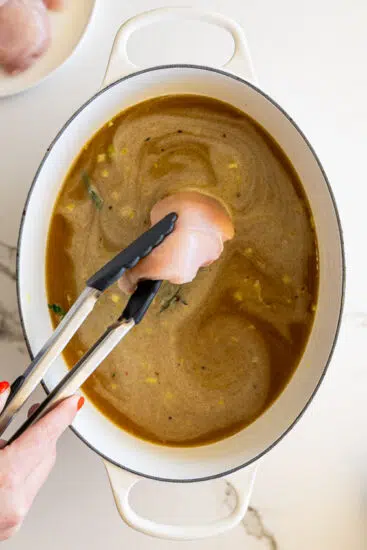 Chicken breasts put into chicken stock in white pot.