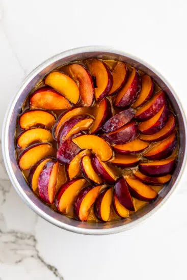 Plums packed into a cake pan on top of caramel sauce.