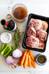 Ingredients for slow braised lamb neck stew on a white surface.