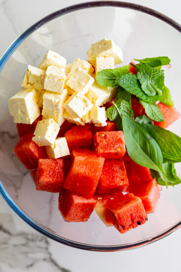 Ingredients for watermelon feta salad in a large glass mixing bowl.
