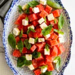 Watermelon salad with feta cheese with fresh basil in a blue and white serving platter.