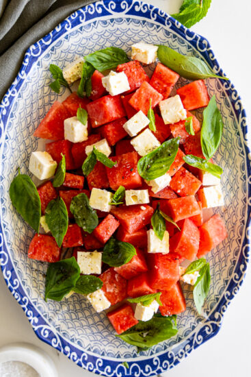 Cubed watermelon and feta cheese in a blue and white serving platter with fresh basil.