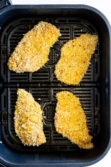 Breaded chicken cutlets in air fryer basket.